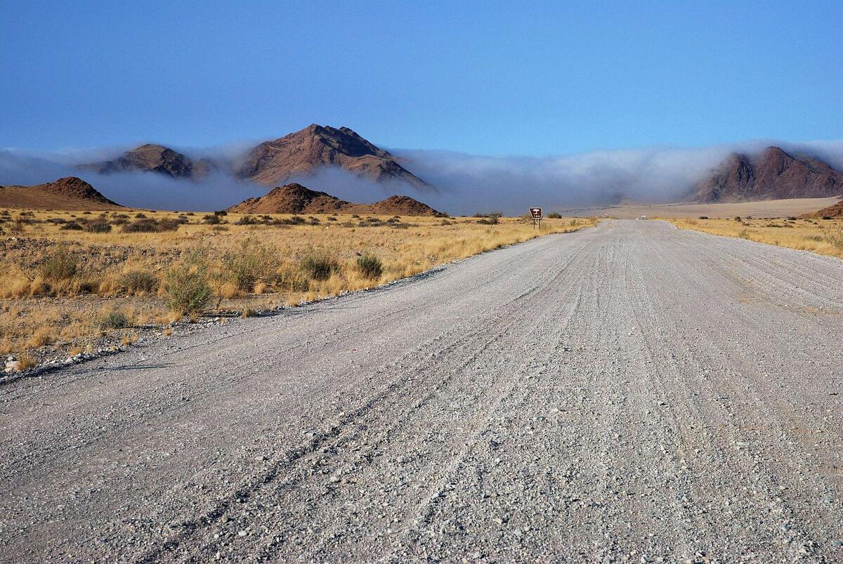 A gravel road crossing the Namibian desert towards distant mountains